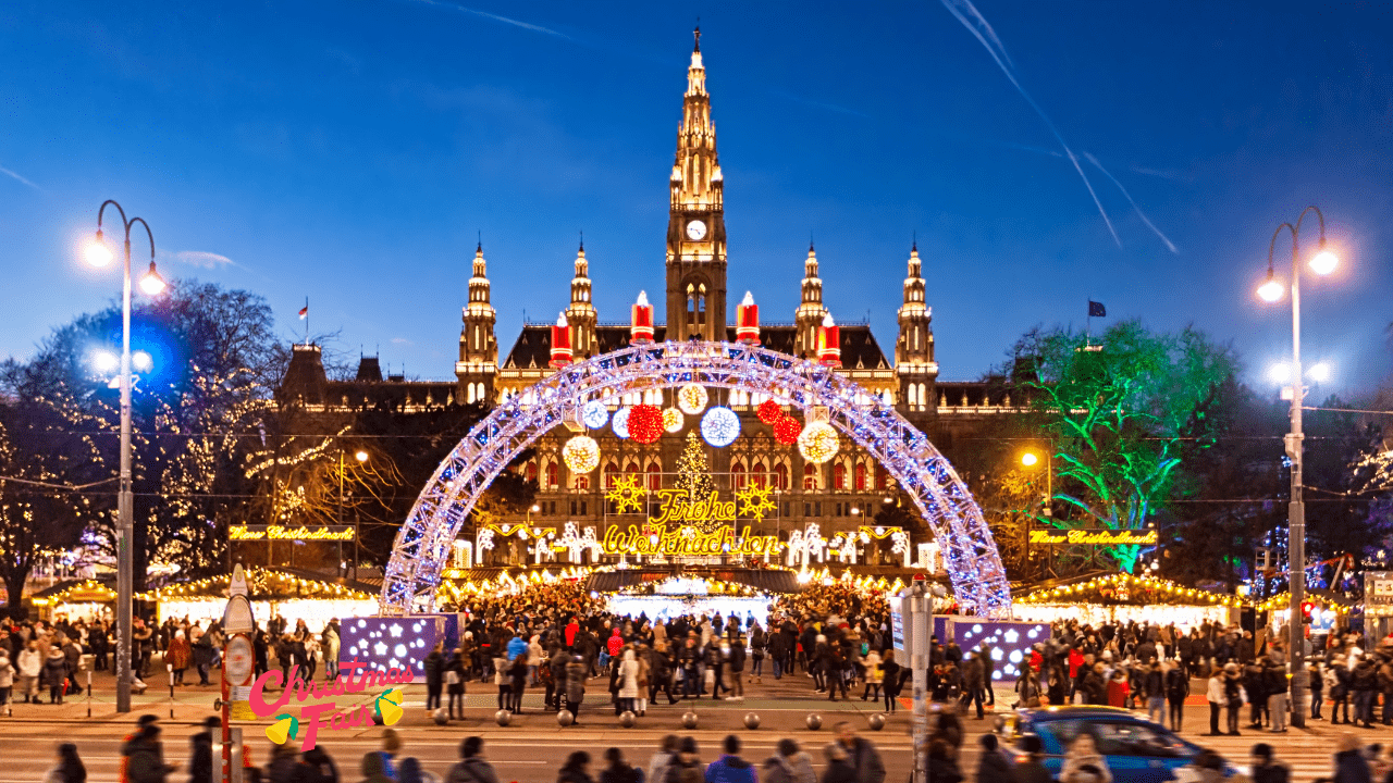 A wide-angle view of a bustling European Christmas market at twilight. Traditional wooden stalls line a historic town square, their roofs dusted with snow and adorned with strings of warm lights. A magnificent Christmas tree stands centrally illuminated, while ornate historic buildings frame the background. Shoppers navigate between stalls selling ornaments, crafts, and seasonal treats, their silhouettes backlit by the golden glow of market lights against the darkening sky. The scene captures the quintessential charm of European holiday traditions. #PragueChristmasMarket #OldTownSquarePrague #BudapestChristmas #VörösmartySquare #VisitPrague #VisitBudapest #PragueMoments #BudapestLife #ChristmasSeason #WinterHolidays #DecemberMagic #HolidayMagic #ChristmasTime